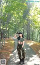 A woman in a military uniform standing on a path in the woods.