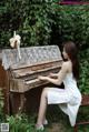 A woman in a white dress sitting on a bench next to a piano.