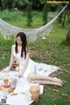 A woman in a white dress sitting on a blanket in the grass.