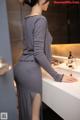 A woman in a gray dress standing in front of a sink.