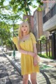 A woman in a yellow dress standing on a sidewalk.