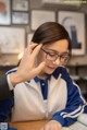 A woman wearing glasses sitting at a table with a book.