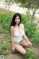 A woman in a white tank top sitting on the ground.