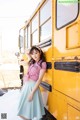 A woman leaning against a yellow school bus in the snow.