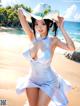 A woman in a white dress and hat on a beach.