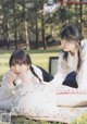 Two young women sitting on a blanket in the grass.