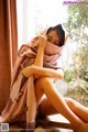 A woman sitting on a window sill wrapped in a blanket.