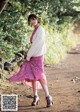 A woman in a pink skirt is walking down a dirt road.