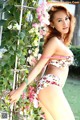 A woman in a bikini posing in front of flowers.