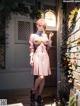 A woman in a pink dress standing in front of a brick wall.