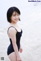 A woman in a black bathing suit standing on a beach.