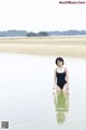 A woman in a black bathing suit standing in the water.