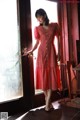 A woman standing in front of a door wearing a red dress.