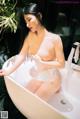 A woman in a white lingerie sitting in a bathtub.