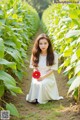 A woman in a white dress holding a red flower.