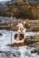 A woman sitting on a rock in the water holding a sword.