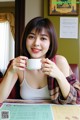 A woman sitting at a table holding a cup of coffee.