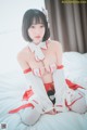 A woman in a red and white outfit sitting on a bed.