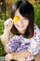 A woman sitting in a field of flowers holding a yellow flower.