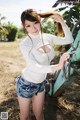 A woman in a white top and denim shorts posing in front of a tractor.